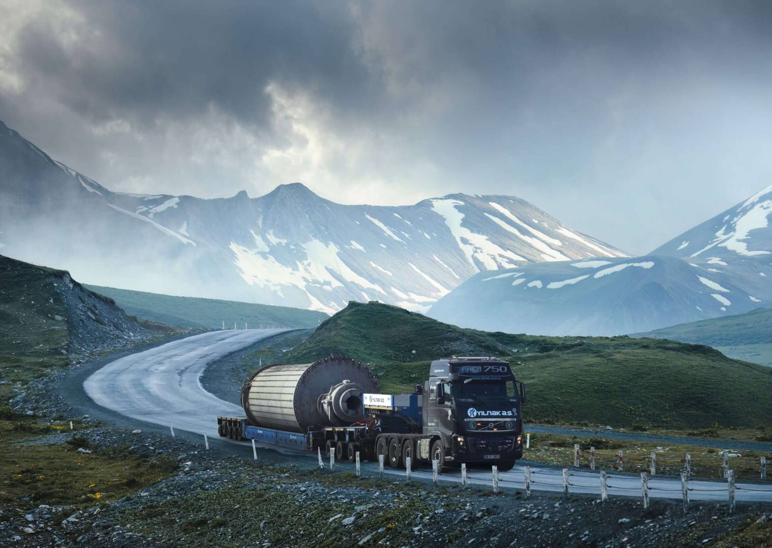 Large,White,Transport,Truck,Transporting,Commercial,Cargo,In,Semi,Trailer Large white transport truck transporting commercial cargo in semi trailer running on turning way highway road with scenic mountains mountaineous scenery in background.